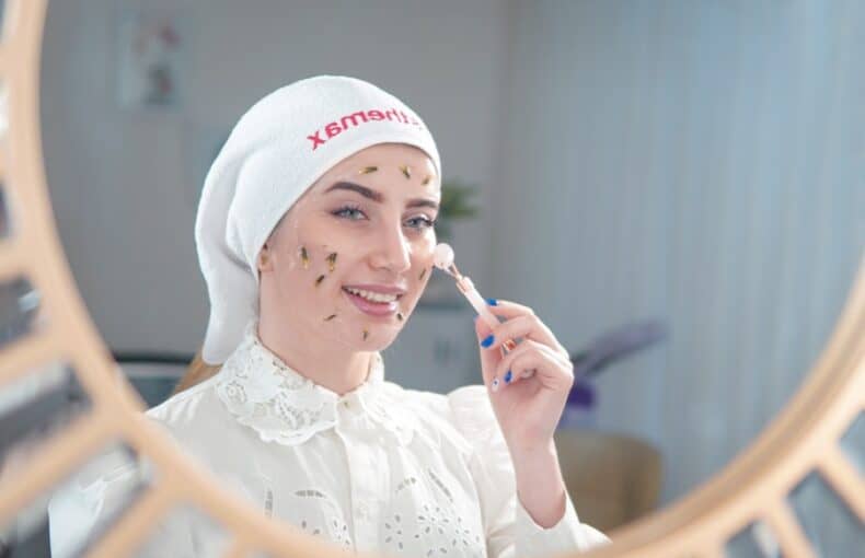 Woman applying skincare treatment with a dropper, smiling in a mirror.